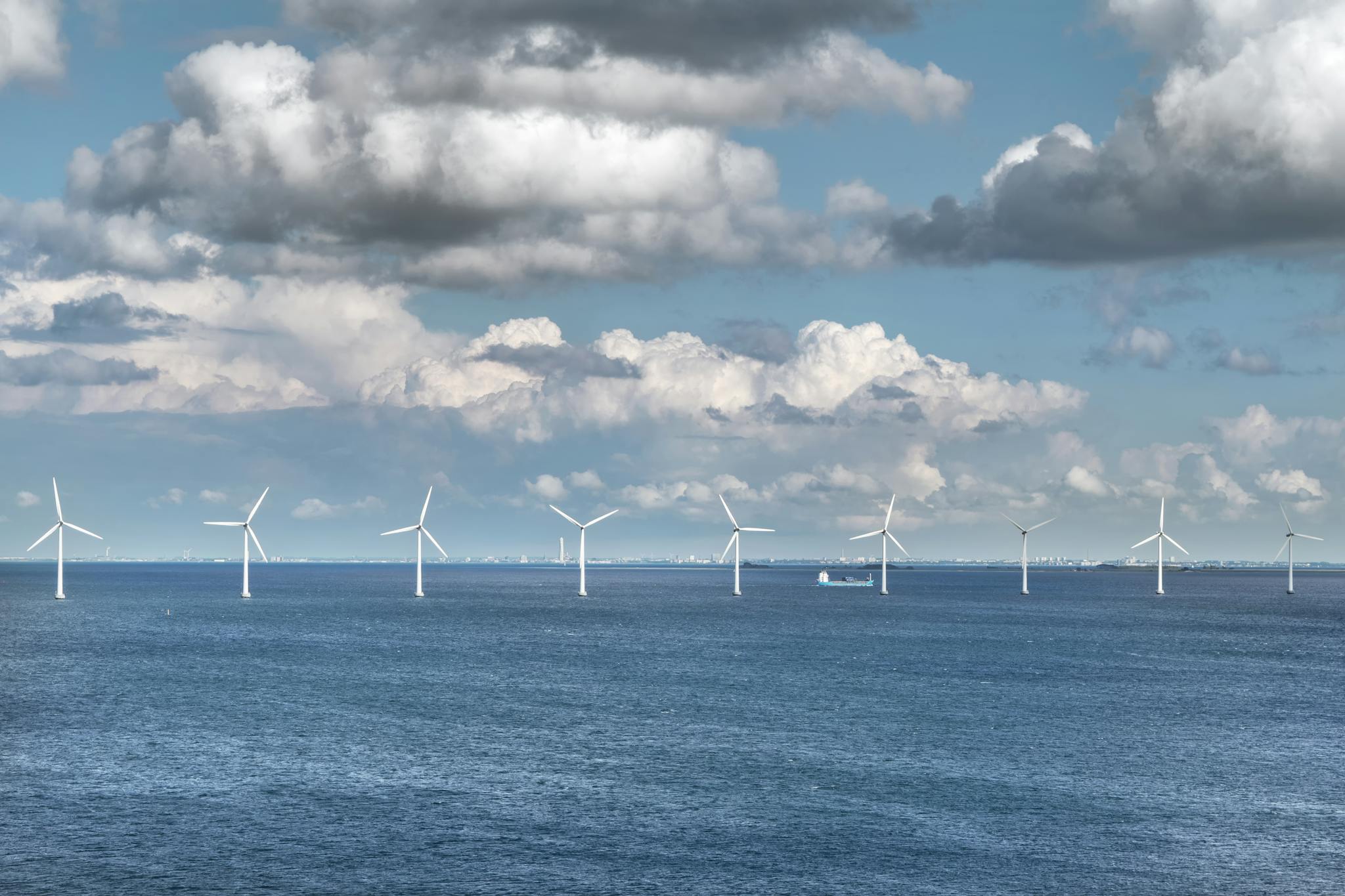 A serene view of offshore wind turbines generating renewable energy under a blue sky with scattered clouds.